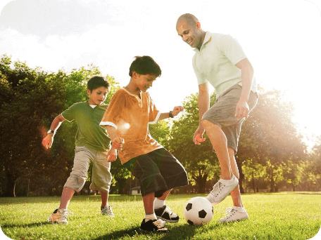Un padre jugando al fútbol con sus dos hijos en una tarde soleada
